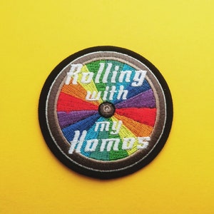 Peut inclure: Un patch rond brodé aux couleurs de l'arc-en-ciel avec le texte "Rolling with my Homos" en blanc.