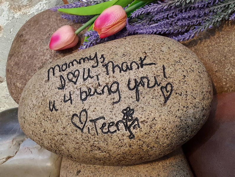 以下が含まれることがあります： 黒いインクで「Mommy I love you Thank you 4 being you」と書かれた、茶色の楕円形の石。石には小さな花とハートも描かれている。