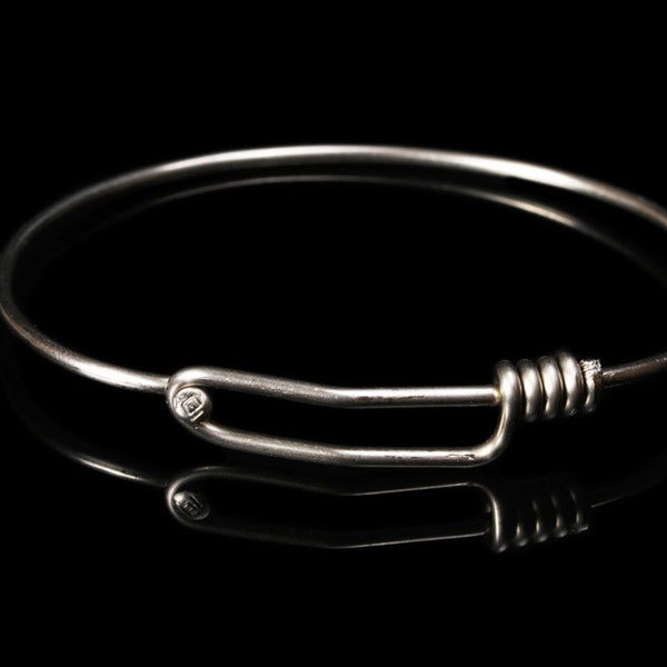 Könnte beinhalten: Ein silbernes Armreif-Armband mit einem einfachen, gedrehten Verschluss.