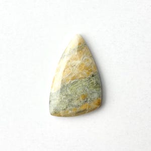 May include: A triangular-shaped gemstone with a polished surface. The stone features a blend of colors, including cream, yellow, and green, with a marbled appearance. The gemstone is set against a white background.