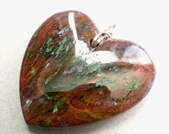 Puede incluir: Un colgante en forma de corazón hecho de jaspe verde, marrón y blanco pulido. El colgante tiene una anilla de plata para sujetar una cadena.