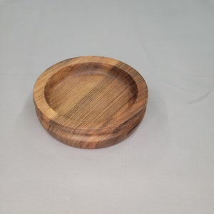Puede incluir: Un tazón de madera redondo con veta de madera marrón oscuro. El tazón está hecho de una sola pieza de madera y tiene un acabado liso y pulido.
