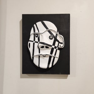 May include: A black and white abstract face sculpture with a geometric pattern. The sculpture is mounted on a black background.
