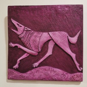 Peut inclure: Sculpture en bas-relief magenta d'un chien courant, gueule ouverte. Le chien présente des motifs détaillés sur son corps et se détache sur un fond magenta foncé texturé. L'œuvre est montée sur une surface carrée et texturée.