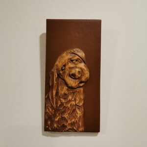 Peut inclure: Une plaque murale en bois brun avec une image sculptée d'une tête de chien. Le chien a un pelage brun et blanc et regarde sur le côté.