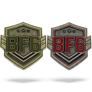 May include: Two shield-shaped metal pins. One is gold with olive green text and the other is silver with red text. Both pins have the text "BF6" and three stars at the top. The pins have a military-style design.