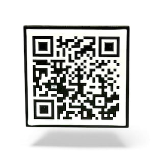 May include: A square QR code with a black frame and a white interior. The code itself is made up of black geometric patterns. The image is well-lit, with a subtle shadow beneath the square.