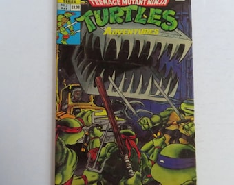 Puede incluir: Portada del cómic Teenage Mutant Ninja Turtles Adventures con las cuatro tortugas en acción contra un gran monstruo metálico con dientes. La portada es amarilla, verde, negra y roja.