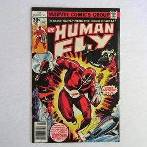 May include: A vintage comic book cover featuring "The Human Fly" in a dynamic pose. The cover is predominantly red and black, with the title in large, bold letters. The artwork depicts a superhero battling enemies, with the text "First Fantastic Issue!"