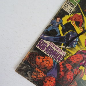Pu&ograve; includere: Una copertina di fumetto vintage con un supereroe in costume blu e un cattivo in costume rosso e giallo. Il testo della copertina recita "...Stranded in Sub-Atomica!"