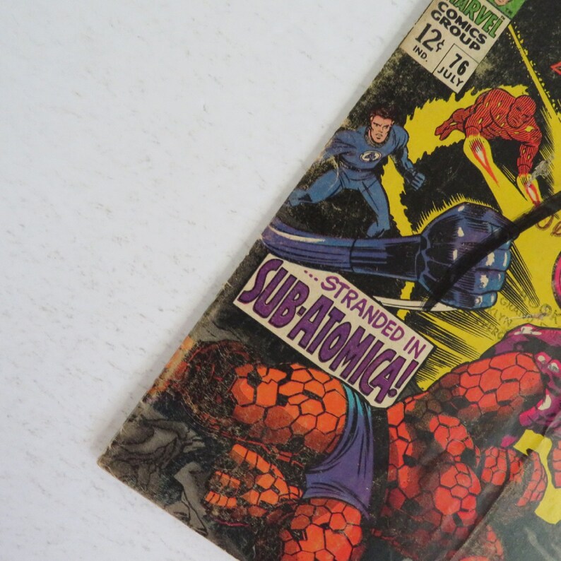 Pu&ograve; includere: Una copertina di fumetto vintage con un supereroe in costume blu e un cattivo in costume rosso e giallo. Il testo della copertina recita "...Stranded in Sub-Atomica!"