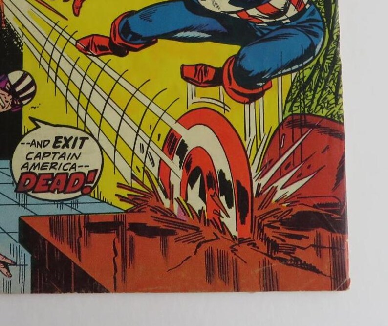 Puede incluir: Una p&aacute;gina de c&oacute;mic con Captain America, un superh&eacute;roe, con un traje rojo, blanco y azul. Est&aacute; volando por el aire con su escudo, que gira y deja un rastro de luz. El texto en la p&aacute;gina dice "--and EXIT CAPTAIN AMERICA-- DEAD!"