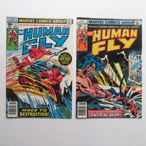 May include: Two vintage Marvel Comics featuring "The Human Fly." Issue 2 shows a red-suited hero battling Ghost Rider, with the text "Race to Destruction!" Issue 5 depicts a muscular figure with blue hair. The comics are from the 1970s.
