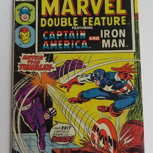 Puede incluir: Una portada de c&oacute;mic con Captain America y Iron Man. La portada es amarilla con detalles en rojo, blanco y azul. El t&iacute;tulo es "Marvel Double Feature" y el lema es "Enter the Tumbler".