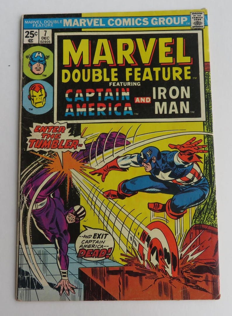 Puede incluir: Una portada de c&oacute;mic con Captain America y Iron Man. La portada es amarilla con detalles en rojo, blanco y azul. El t&iacute;tulo es "Marvel Double Feature" y el lema es "Enter the Tumbler".