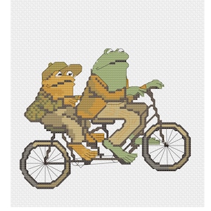 Puede incluir: Dos ranas montando en bicicleta. La rana de delante es verde y lleva una chaqueta marrón. La rana de detrás es marrón y lleva una chaqueta verde y un sombrero marrón.