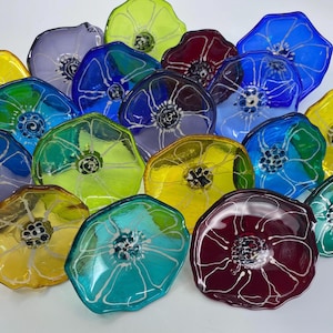 May include: Assortment of colorful glass flower-shaped ornaments with white painted details. The ornaments are made of glass and have a variety of colors, including blue, green, yellow, purple, and red.