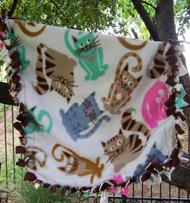 The background is creme with multi-colored cats Small Cat Throw in 100/% Glacier poly fleece What a fun cat throw! Size is 24x 24.