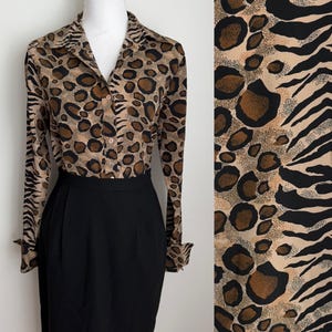 May include: A long-sleeved button-down shirt featuring a tan, brown, and black animal print pattern with a mix of leopard spots and zebra stripes, paired with a solid black high-waisted skirt. The shirt has a pointed collar and buttoned cuffs.