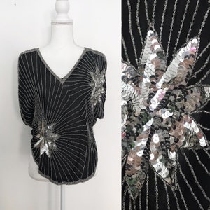 May include: A black sequined top with silver star-shaped embellishments. The top has a V-neck and short sleeves.