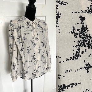 May include: A white long-sleeved blouse with a black abstract print. The blouse has a collared neckline and button closure.