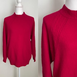 May include: A vibrant red sweater with a mock neck collar. The long-sleeved top is displayed on a white mannequin. The sweater has a ribbed texture and a close-up shows the shoulder seam detail. A stylish addition to any wardrobe.