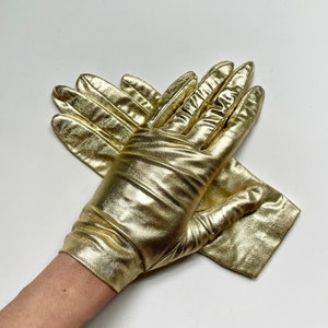 May include: A pair of gold-colored gloves made of a shiny, satiny material. The gloves are folded in half, with the fingertips of one glove tucked into the palm of the other.
