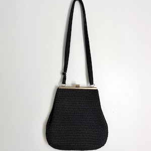 Puede incluir: Un bolso de mano negro tejido a ganchillo con una forma estructurada y un cierre de marco metálico en tono dorado. El bolso incluye una correa de hombro negra fina y ajustable sujeta al marco con anillas metálicas plateadas y una hebilla.