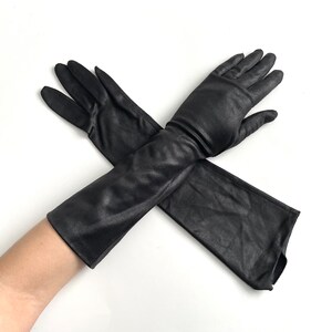 May include: A pair of long black satin gloves. The gloves are crossed over each other and the fingertips are visible.