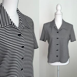 May include: A black and white striped button-down shirt with short sleeves. The shirt has a collared neckline and is displayed on a mannequin. The stripes are horizontal and evenly spaced. The shirt is buttoned up with black buttons.