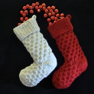 Könnte beinhalten: Zwei gestrickte Weihnachtsstrümpfe, einer weiß und einer rot, mit einer roten und weißen Perlenkette, die über die Oberseite gelegt ist.