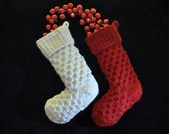 May include: Two knitted Christmas stockings, one white and one red, with a red and white beaded garland draped over the top.