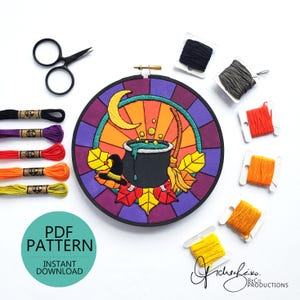 May include: A circular embroidery hoop with a Halloween design, including a cauldron, witch's hat, and broom. The design is surrounded by autumn leaves and a crescent moon. Embroidery floss and scissors are also visible in the image.