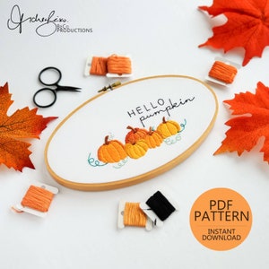 Könnte beinhalten: Ein Stickrahmen mit der Aufschrift "Hello Pumpkin" und gestickten orangefarbenen Kürbissen. Das Bild zeigt orangefarbenes Garn, eine Schere und Herbstblätter. Ein PDF-Muster ist ebenfalls verfügbar.