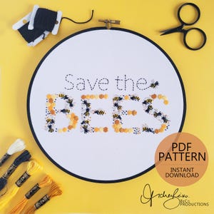 May include: A white embroidery hoop with the words "Save the Bees" stitched in black and yellow thread. The word "BEES" is designed with bee and honeycomb patterns. Black scissors, thread, and embroidery floss are in the background.