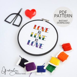 May include: A white embroidery hoop with the words "Love is Love" stitched in rainbow colours. The hoop is surrounded by embroidery floss in various colours, including red, orange, yellow, green, blue, purple, and black.