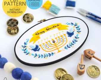 May include: A white embroidery hoop with a blue and yellow embroidered design of a menorah, candles, and the text "Happy Hanukkah". The hoop is surrounded by blue and white yarn, gold coins with a Star of David, and wooden dreidels.