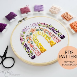 Może przedstawiać: Kolorowy wzór haftu przedstawiający tęczę z kwiatowymi detalami, idealny dla początkujących hafciarek. Wzór jest dostępny jako natychmiastowy plik PDF do pobrania.
