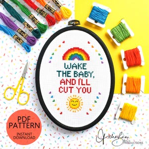 May include: An oval cross-stitch embroidery with the text "Wake the baby, and I'll cut you" and a rainbow design. The image includes colourful embroidery floss, scissors, and a PDF pattern download graphic.
