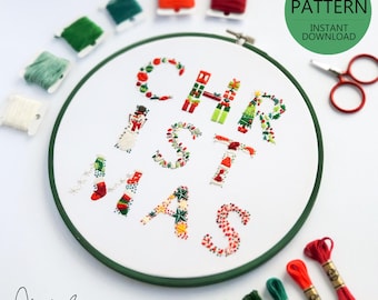 Könnte beinhalten: Ein weißer Stickrahmen mit einem grünen Außenring, der ein farbenfrohes Stickmuster des Wortes "WEIHNACHTEN" zeigt. Das Design enthält verschiedene Weihnachtselemente wie Ornamente, Schneeflocken und einen Schneemann. Der Rahmen ist von bunten Stickgarnrollen umgeben.