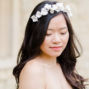 May include: A woman with long dark hair wearing a white flower crown. The crown is made of small white flowers.