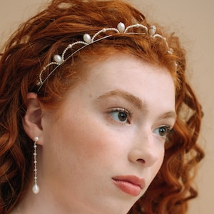 May include: A silver tiara with pearl detailing and matching drop earrings. The tiara has a thin, curved band with small pearls and larger, teardrop-shaped pearls. The earrings feature a string of small pearls leading to a larger pearl, creating an elegant look.