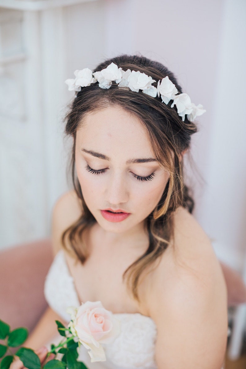 May include: A bride wearing a white strapless dress and a flower crown with a single pink rose in her hand.