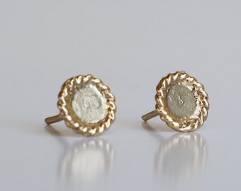 May include: A pair of gold-toned stud earrings with a circular design. The earrings have a textured, rope-like border.