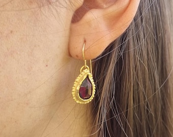 May include: Gold dangle earrings with a teardrop-shaped red gemstone.