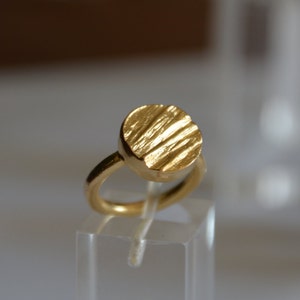 May include: A gold ring with a textured, round top. The ring is made of a smooth, shiny metal.