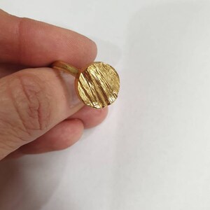 May include: A gold ring with a textured, circular design. The ring is made of a smooth, shiny metal.