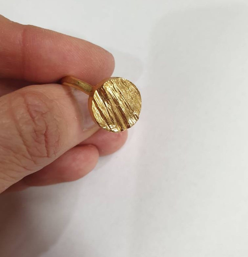 May include: A gold ring with a textured, circular design. The ring is made of a smooth, shiny metal.