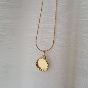 May include: A gold chain necklace with a round pendant. The pendant has a textured, rope-like design around the edge.