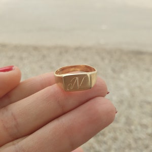 May include: A gold signet ring with a square face and the letter "N" engraved on it.